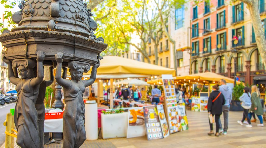 Tourists walk down a pedistrian street in Barcelona, lined by vendor tents.
