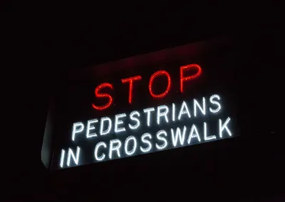 "Stop - Pedestrians in crosswalk" sign in white and red lights.