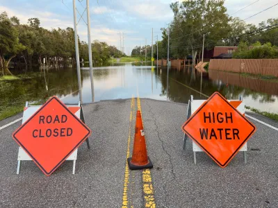Orange and black "Road Closed" and "High Water" signs blocking a flooded roadway in Florida after a hurricane.