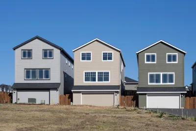 Three new single-family homes in a row on a lot with no trees.