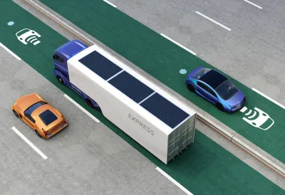 Rendering of truck and cars driving on green electric vehicle charging roadway lane.