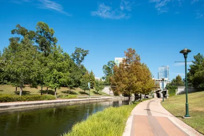 Paved walking path next to canal in The Woodlands, Texas with office buildings in background.