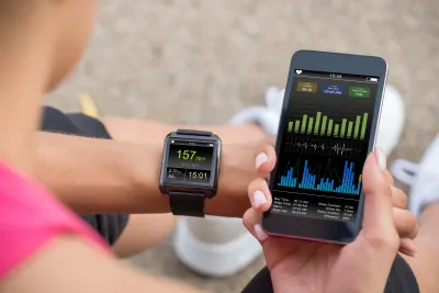Close-up of person holding up phone and looking at their smart watch displaying fitness data