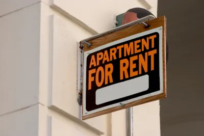 Close-up of black, white, and orange APARTMENT FOR RENT sign on building.