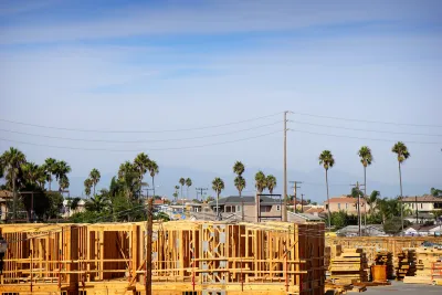 Wood-frame apartment building under construction with tall palm trees and power lines in background.