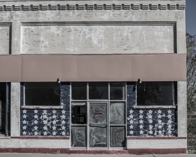 Faded image of vacant storefront in rural area with American flag stars painteind on windows.