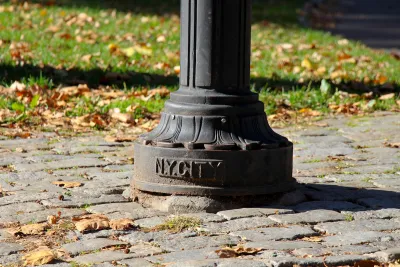 CLose-up of bottom of lamp post with NY CITY plaque on cobblestone sidewalk in Central Park, New York City.