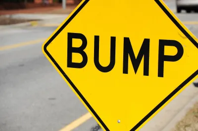 Close-up on yellow sign with black 'BUMP' letters indicating speed bump ahead.