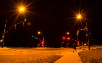 Intersection with stoplights at night with one pedestrian waiting to cross.