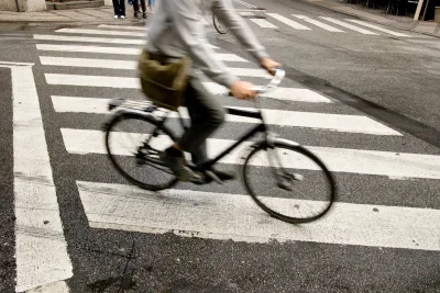 Person on bike riding across zebra crosswalk in city.