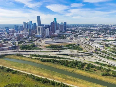 Aerial view of massive freeway interchange with downtown Houston skyline in background.