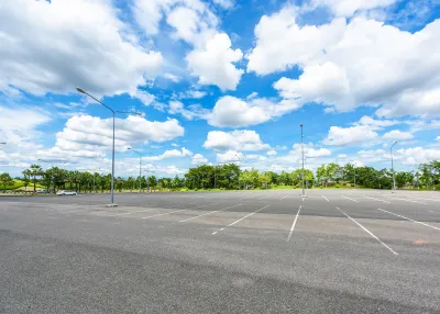 Empty large outdoor parking lot with green trees in background.