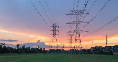 Electricity towers against sunset sky with green trees in background.