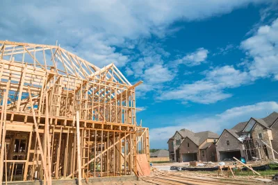 Wood-framed houses under construction with brick-covered completed homes in background.