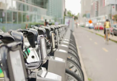 Close-up of silver Bixi bike share bikes parked at a station in Montreal, Quebec, Canada with blurred person on bike riding away in background.
