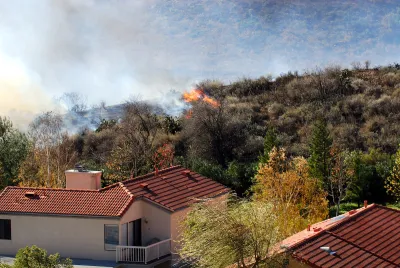 Wildfire approaching stucco house with red tile roof.