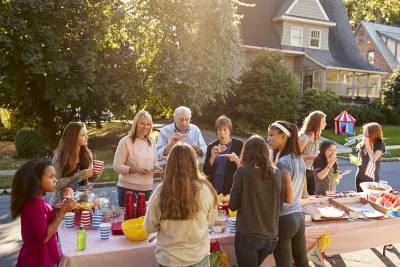 Group of people standing around a table with food in front of homes during a block party.