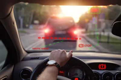 Close-up of car steering wheel and dashboard with driver's hand on steering wheel and illustration of automatic braking system on windshield with 'STOP' graphic.