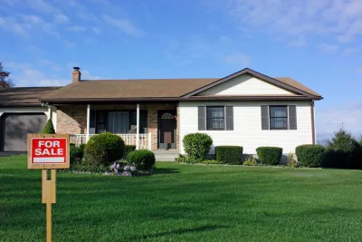 Small home with For Sale sign on green lawn.