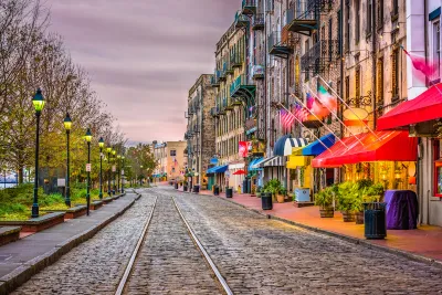 Cobblestone street with streetcar line, row of vintage streetlights on left, and colorful restaurant and shop awnings on right on River Street in Savannah, Georgia.