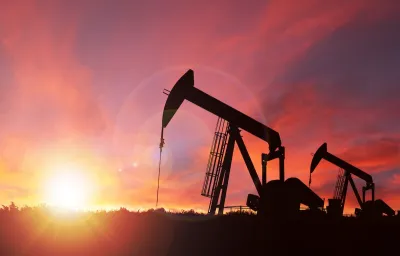 Oil well pumpjack sillhouetted against a bright pink sunset sky.