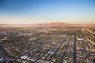 Aerial view of sprawling Las Vegas suburbs at golden hour with desert mountain in background.