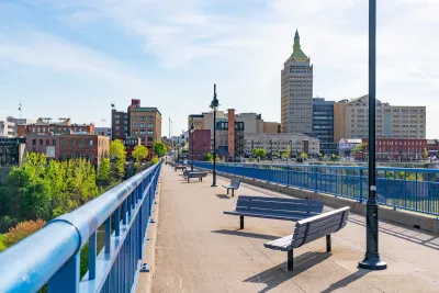 Pedestrian bridge with benches in Rochester, New York with brick buildings in background.