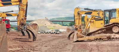 Three yellow excavators at a road construction site with elevated roadway in background.