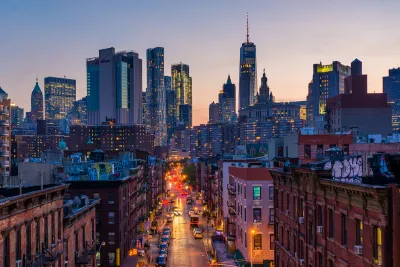 View down New York City street with rick buildings in foreground and modern skyline in background at sunset.