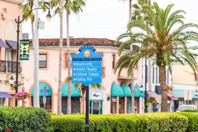 Street sign in Venice, Florida planned community with pink Italianate buildings and palm trees in background.