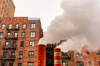 Orange and white steam pipes in New York City releasing white steam against background of red brick buildings.