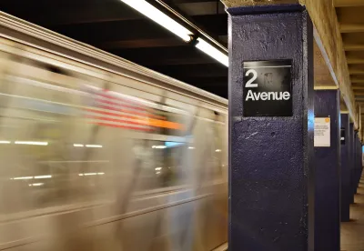 View of 2nd Avenue sign on concrete column on subway platform with blurred train speeding past in New York City.