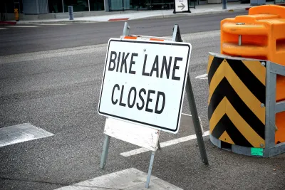 "Bike Lane Closed" A-frame sign on street with yellow and black barricade behind it.