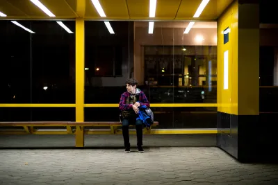 Yellow bus shelter with one young person sitting on bench at night.