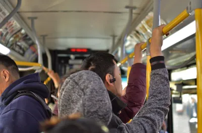 Interior of busy city bus with people standing, holding on to top bar.