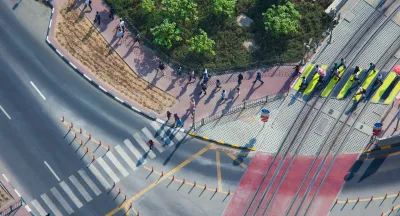 Overhead view of doxens of commuters walking on sidewalk and crossing street in full sun.