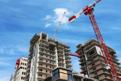 View of top of high-rise apartment building under construction with red and white cranes