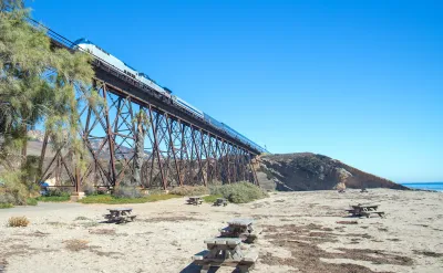 Amtrak train passing over tall trestle bridge on California coast at Gaviota Beach.