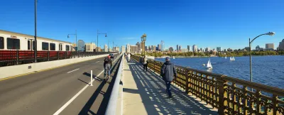 View of Boston skyline from Longfellow Bridge with cyclist riding in bike lane and pedestrian on sidewalk.