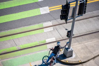 Cyclist pressing crossing button at green painted crosswalk.
