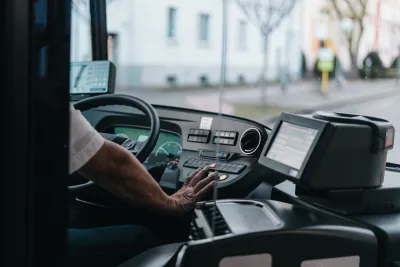 Close-up of bus driver from behind with only hand visible on steering wheel.