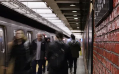 Busy New York City subway platform with blurred people walking in and out of trains and close-up on red brick wall on right.