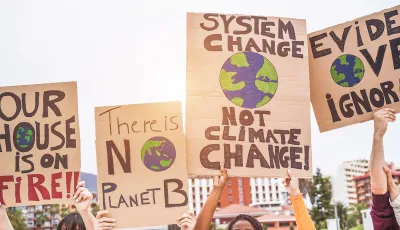 Close-up of signs calling for action on climate change being help up by multiple people outdoors.