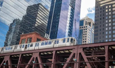 View up at Chicago elevated train line with train passing and glass high-rises in background.
