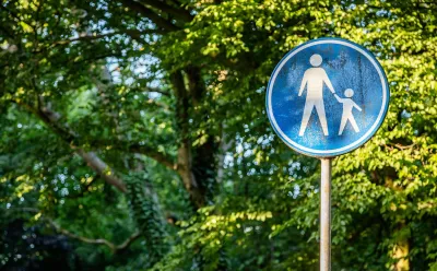 Blue sign with white sillhouettes indicating parent and child crossing street.
