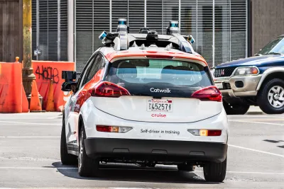 White and red Cruise self-driving car with "Self-driver in training" sign on back
