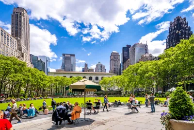 People sitting on lawn chairs in front of green meadow with New York City skyscrapers in background in Bryant Park, New York.