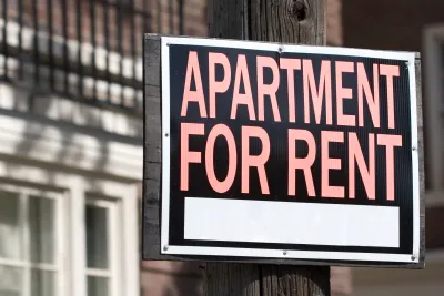 Close-up of "Apartment for rent" sign in red text on black background in front of blurred building