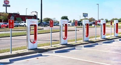 White and red Tesla EV chargers in an open-air parking lot in Corsicana, Texas with Dairy Queen restaurant in background