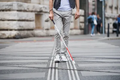 Low view of person with vision impairment cane walking through crosswalk.